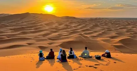 18 days morocco tour from casablanca.Camel caravan trekking across the golden dunes of the Sahara Desert during the 18-Day Morocco Desert and Imperial Cities Tour, with a dramatic sunset in the background.