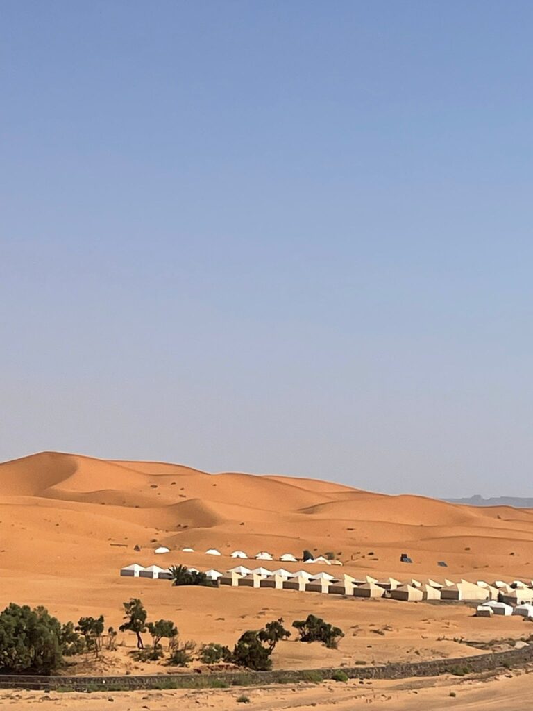 4 Day Desert Tour From Marrakech,Camel trek across the golden Merzouga dunes during a 4-day desert tour from Marrakech. Sunset over the Sahara desert with traditional Berber camp tents on a Marrakech to Merzouga tour. Scenic view of the Atlas Mountains along the route of a 4-day Morocco desert adventure. Historic Kasbah Aït Benhaddou visited during a 4-day Sahara desert tour from Marrakech. Todra Gorge cliffs explored on the way to Merzouga during a 4-day desert tour. Night under the stars at a Berber desert camp on a 4-day Marrakech to Merzouga trip. Travelers walking through the Dades Valley on a 4-day Morocco desert adventure. Sunrise over Erg Chebbi dunes on a camel ride during a 4-day desert tour from Marrakech.